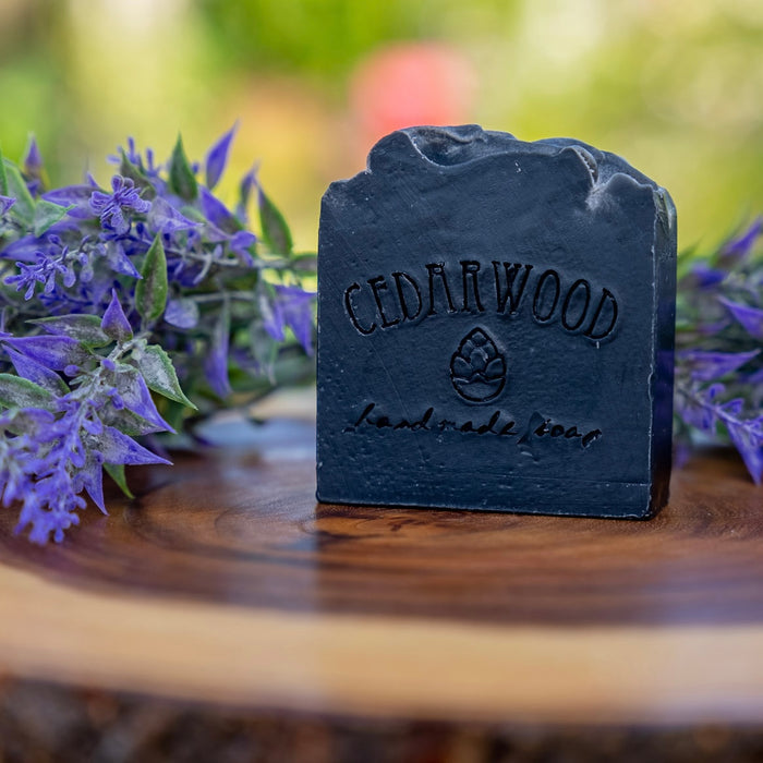Handmade bar Tea Tree Charcoal soap on wood surface surrounded by lavender flowers