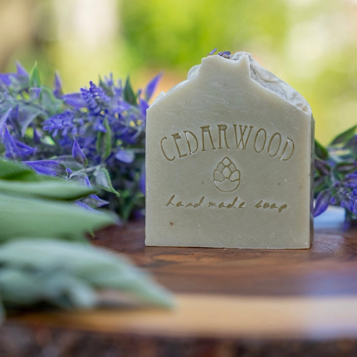 Handmade bar of Laveder Sage soap on wood surface surrounded by lavender flowers