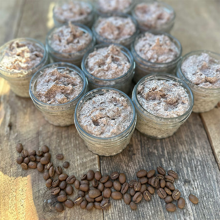 Twelve jars of handmade coffee sugar body scrub with coffee beans in foreground